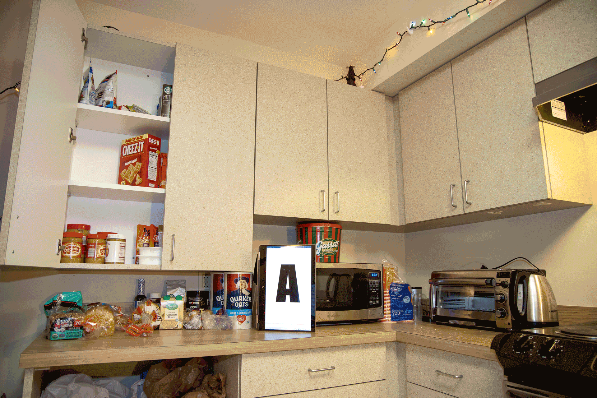 Depicts a kitchen, alternating which cabinet is open, with a computer display spelling out "ART???"