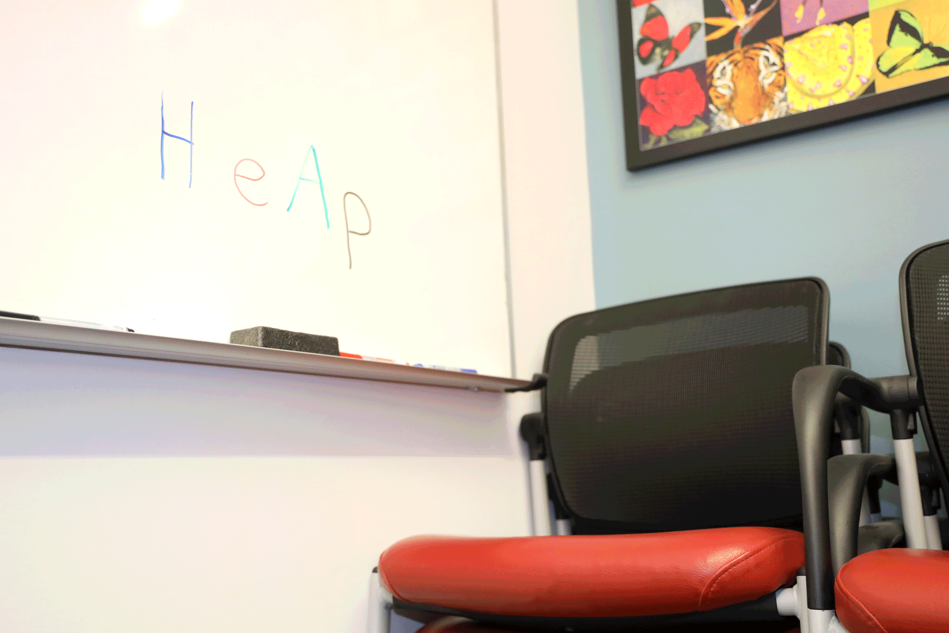 Paper piles up on a chair as text on a whiteboard states "A heap"